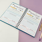 Inside view of the space-themed children's journal, showing two daily journal pages with prompts for gratitude, best moments, and helpful tasks.